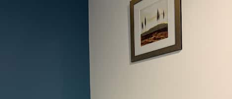 Una cama bien hecha con ropa blanca en una habitación con una pared azul decorativa y un cuadro de paisaje colgado encima.