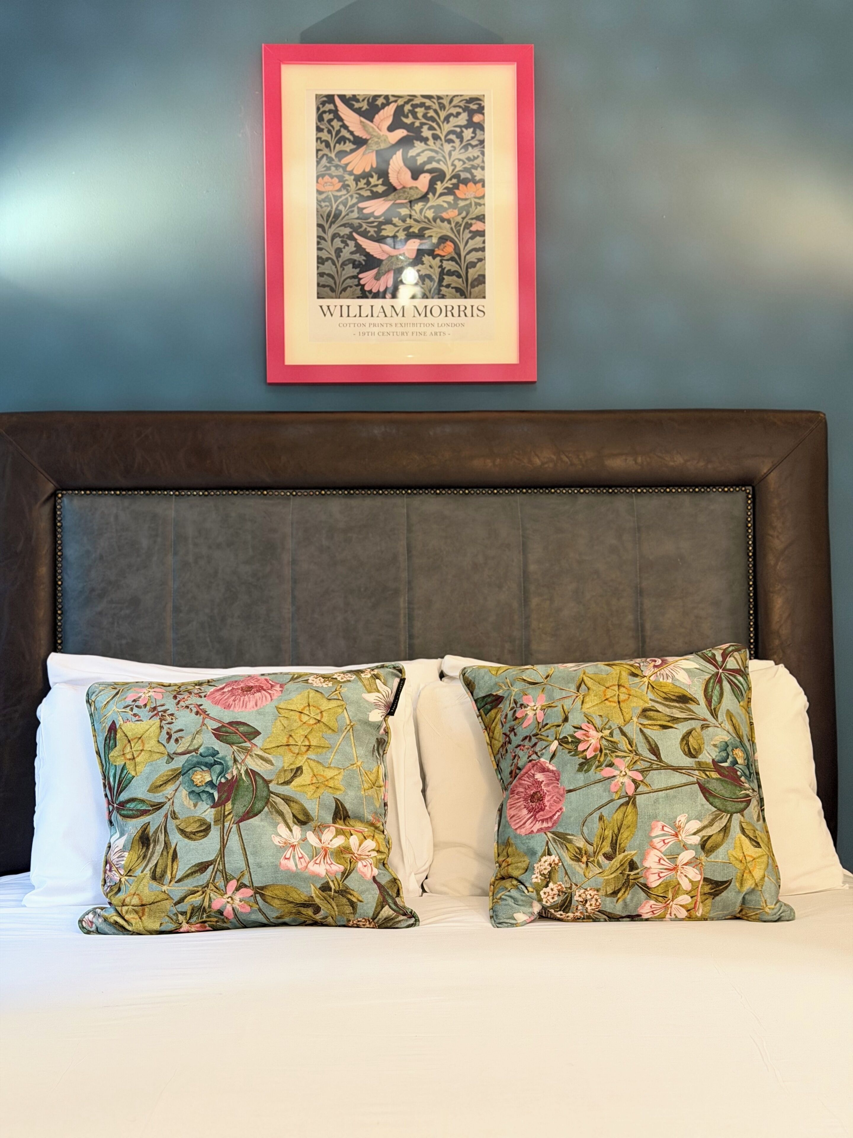 A bed with floral-patterned pillows and a framed artwork above it.