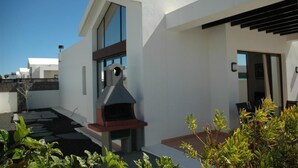 Uma casa moderna com churrasqueira, um alpendre com mesa e um pequeno jardim.