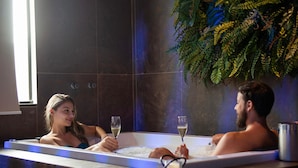 Una pareja en un jacuzzi con vista a una ventana y una planta.
