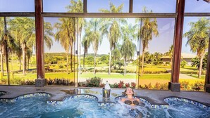Una persona en un jacuzzi con vistas a un campo de golf a través de grandes ventanales.