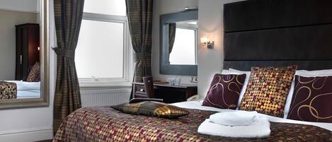 Una habitación de hotel con una cama grande, un escritorio, un espejo y una ventana con cortinas.