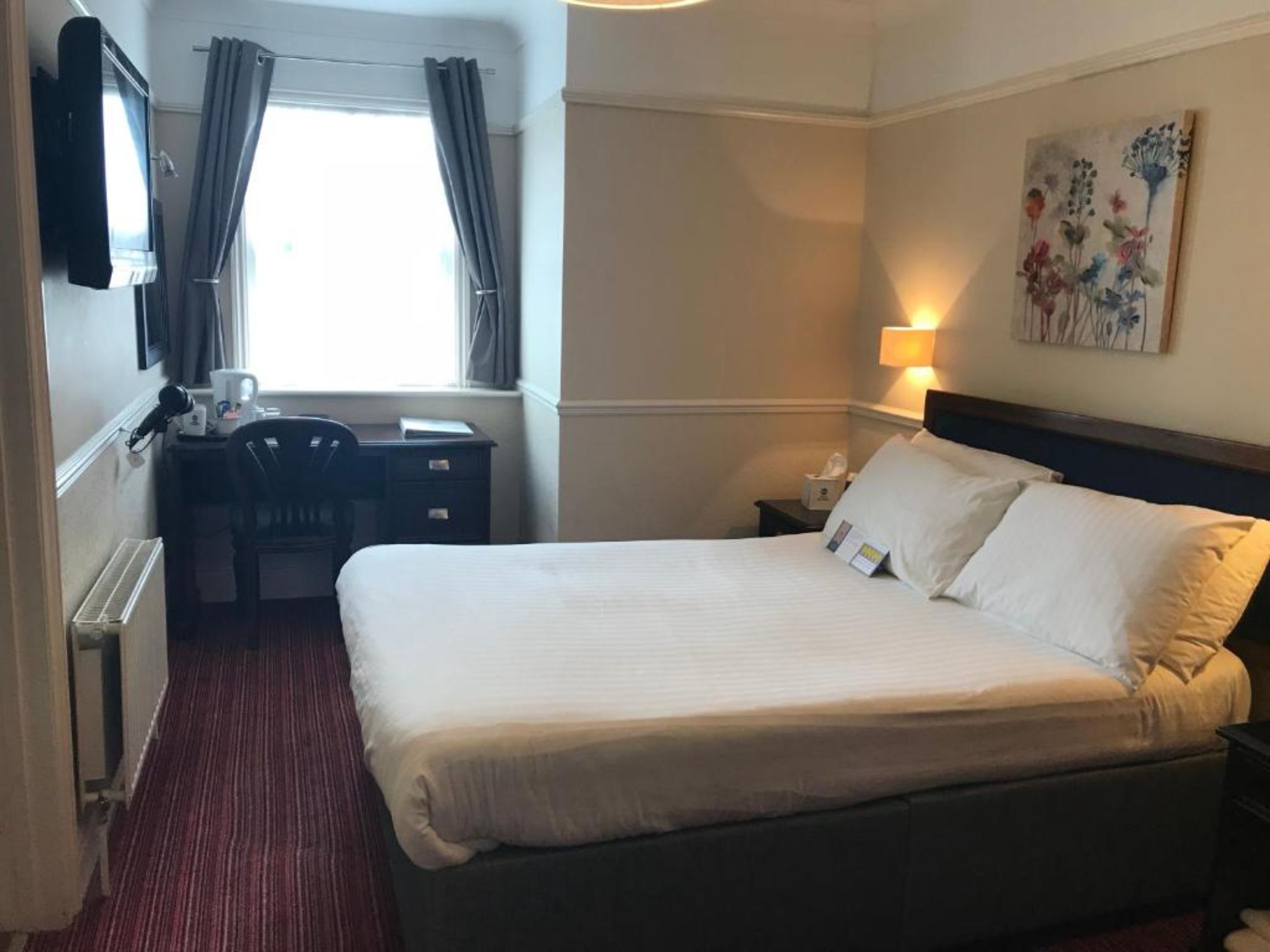 A hotel room with a large bed, a desk with a chair, a flat-screen TV, and a painting on the wall.