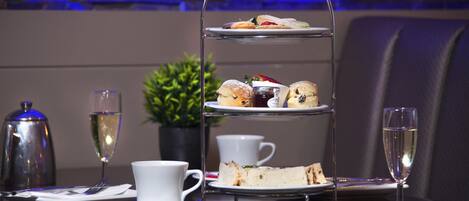 A three-tiered dessert stand with sandwiches and pastries, a coffee cup, a glass of champagne, and a teapot on a table.