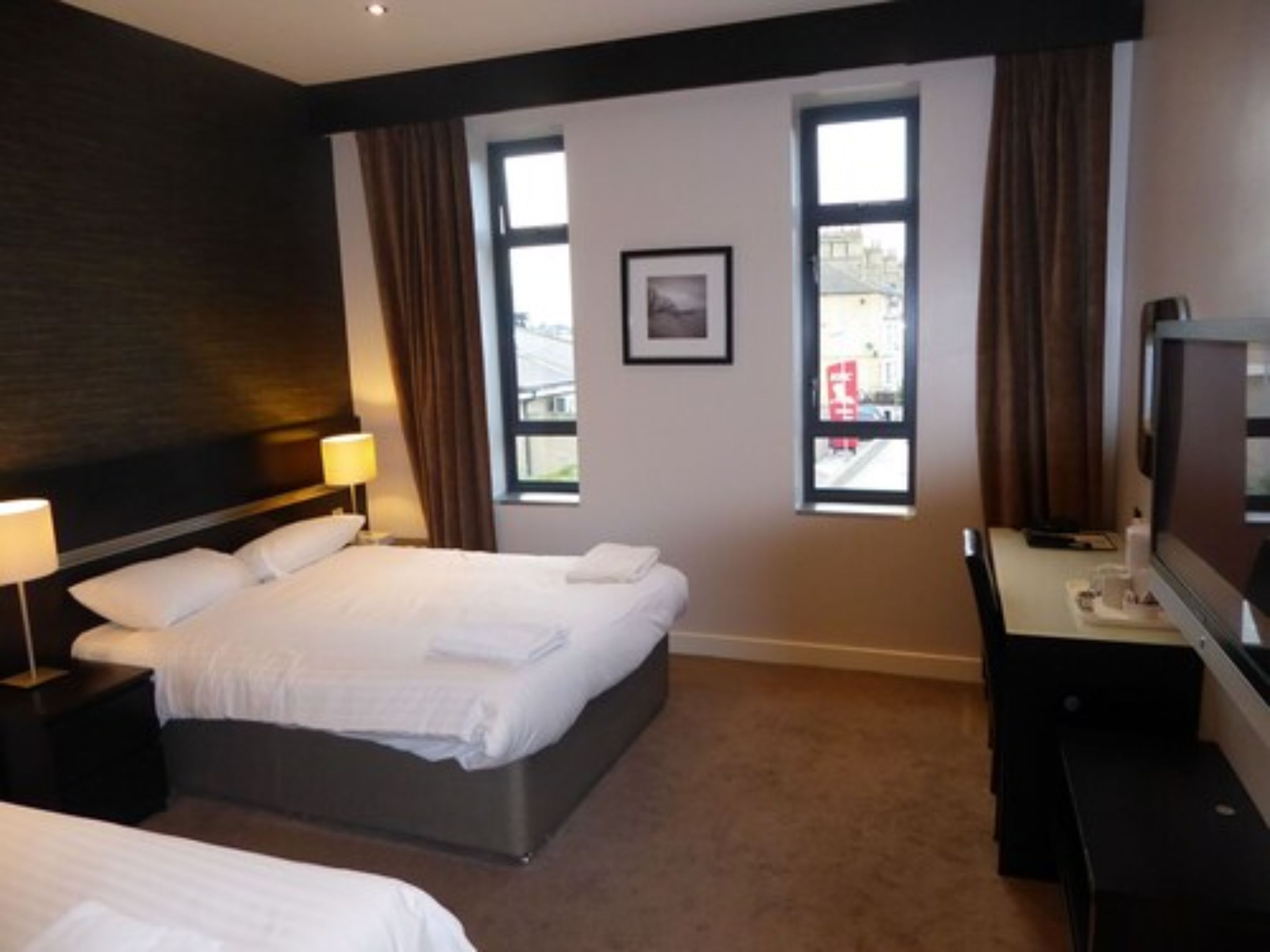 Una habitación de hotel con cama, escritorio con computadora y ventana con cortinas.
