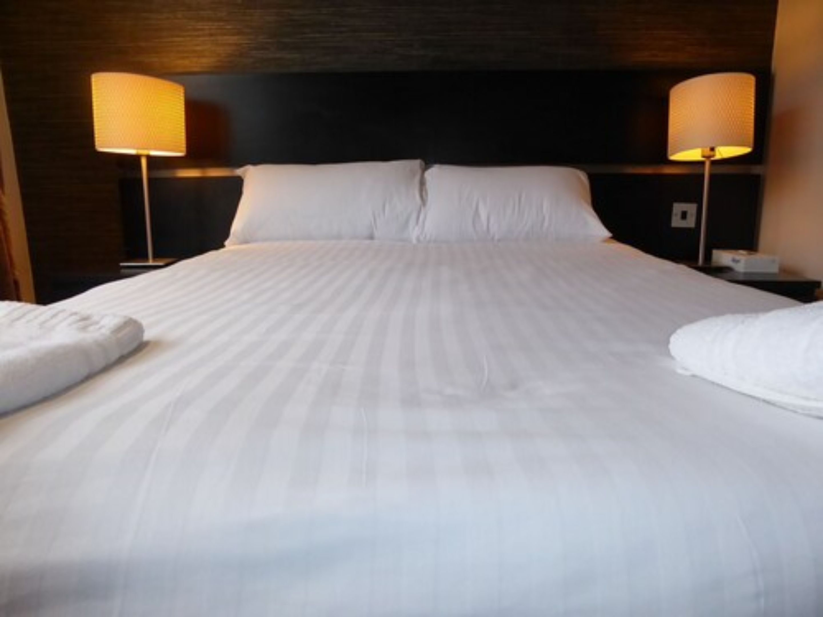 A neatly made bed with white linens and two bedside lamps.