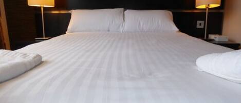 A neatly made bed with white linens and two bedside lamps.