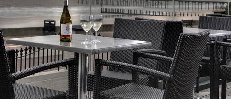 Ein Tisch mit einer Weinflasche und zwei Gläsern, Korbstühle und Blick auf das Meer und den Pier.