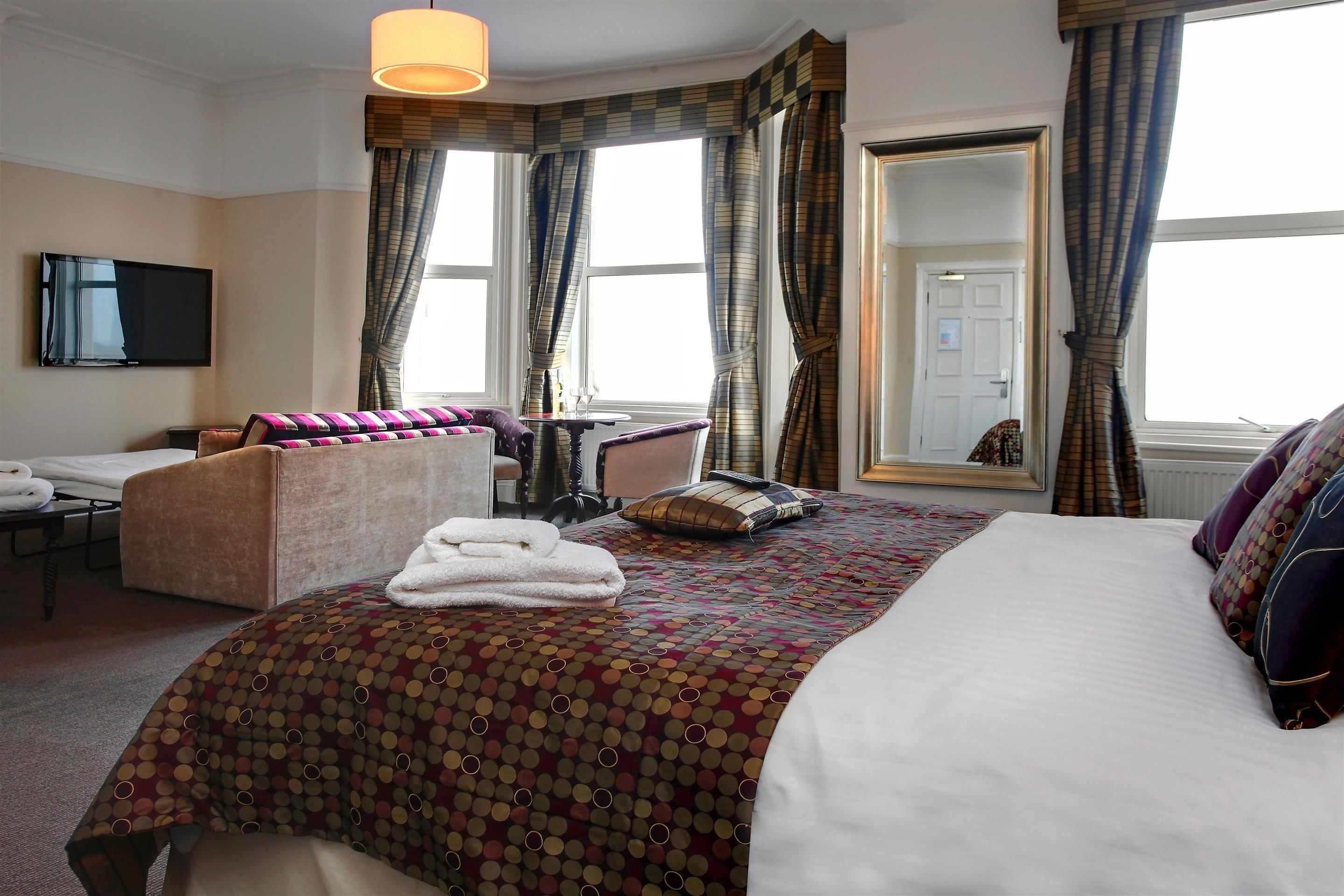 A hotel room with a bed, a sofa, a desk, and a television.