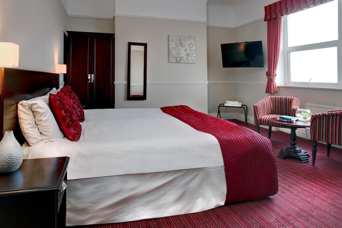 Ein Hotelzimmer mit einem großen Bett, einem Fernseher, einem Sessel und einem Schreibtisch.