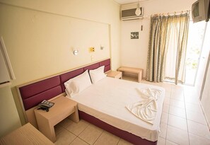 Hotellihuone, jossa on suuri sänky, yöpöytä, pieni työpöytä, ilmastointilaite, televisio ja ikkuna, jossa on verhot.