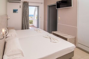 A hotel room with a bed, a TV mounted on the wall, and a view of the sea through an open door. - Megim Hotel (Kantanos-Selino)