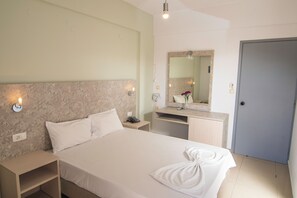 Une chambre d’hôtel comprenant un lit, une table de chevet, une commode et une salle de bain avec un miroir, un lavabo et une serviette.