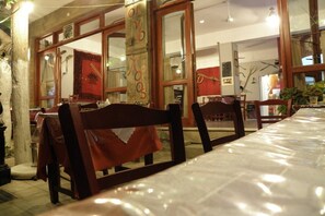 An indoor dining area with wooden chairs and tables, large windows, and a visible door. - Megim Hotel (Kantanos-Selino)