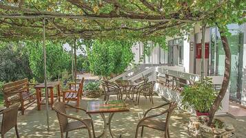 Un patio al aire libre con mobiliario de mimbre, una jardinera de piedra y una pérgola cubierta de enredaderas.