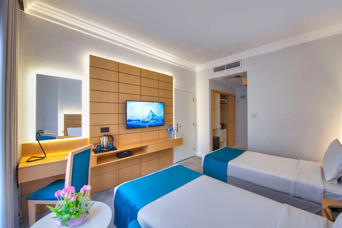A hotel room with two beds, a desk, a TV, and a bathroom visible through an open door.