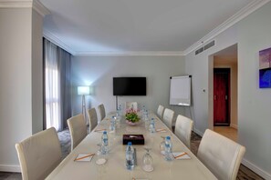 A conference room with a long table, chairs, a TV, a whiteboard, and a floral arrangement. - Lotus Grand Hotel Dubai (Dubai)