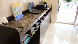 A reception desk with a laptop, a phone, and a map stand. There are brochures and a sign with Japanese text. - Toyoko Inn Tokyo Tozai Line Nishikasai (Tokyo)