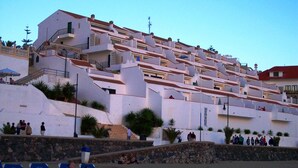 Un hôtel à la façade blanche, doté de nombreux balcons et d’un mur de soutènement en pierre.
