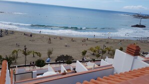 Une plage avec des gens et des parasols, une tour de surveillance des sauveteurs, et une vue sur l’océan.