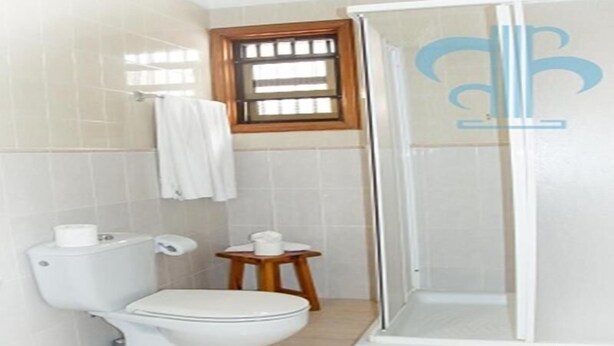 A bathroom with a toilet, a small wooden stool, and a glass-enclosed shower area. - Las Fuentes (Arona)