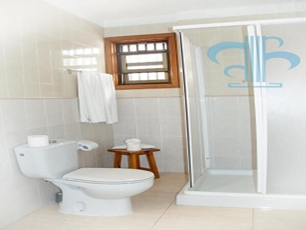 Un baño con inodoro, un taburete de madera pequeño y una zona de ducha con mampara de vidrio.