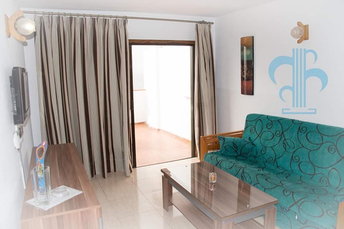 A modern living room with a sofa, a coffee table, and a sliding door leading to a balcony.