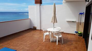 A balcony with a white table and chairs, a beige umbrella, and a view of the ocean.