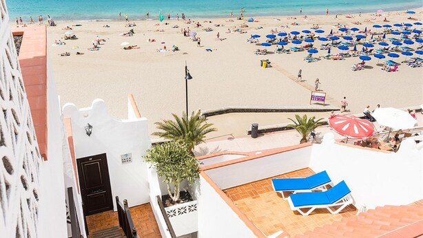 Vue sur la plage depuis le balcon d’un hôtel, avec des transats et des parasols.