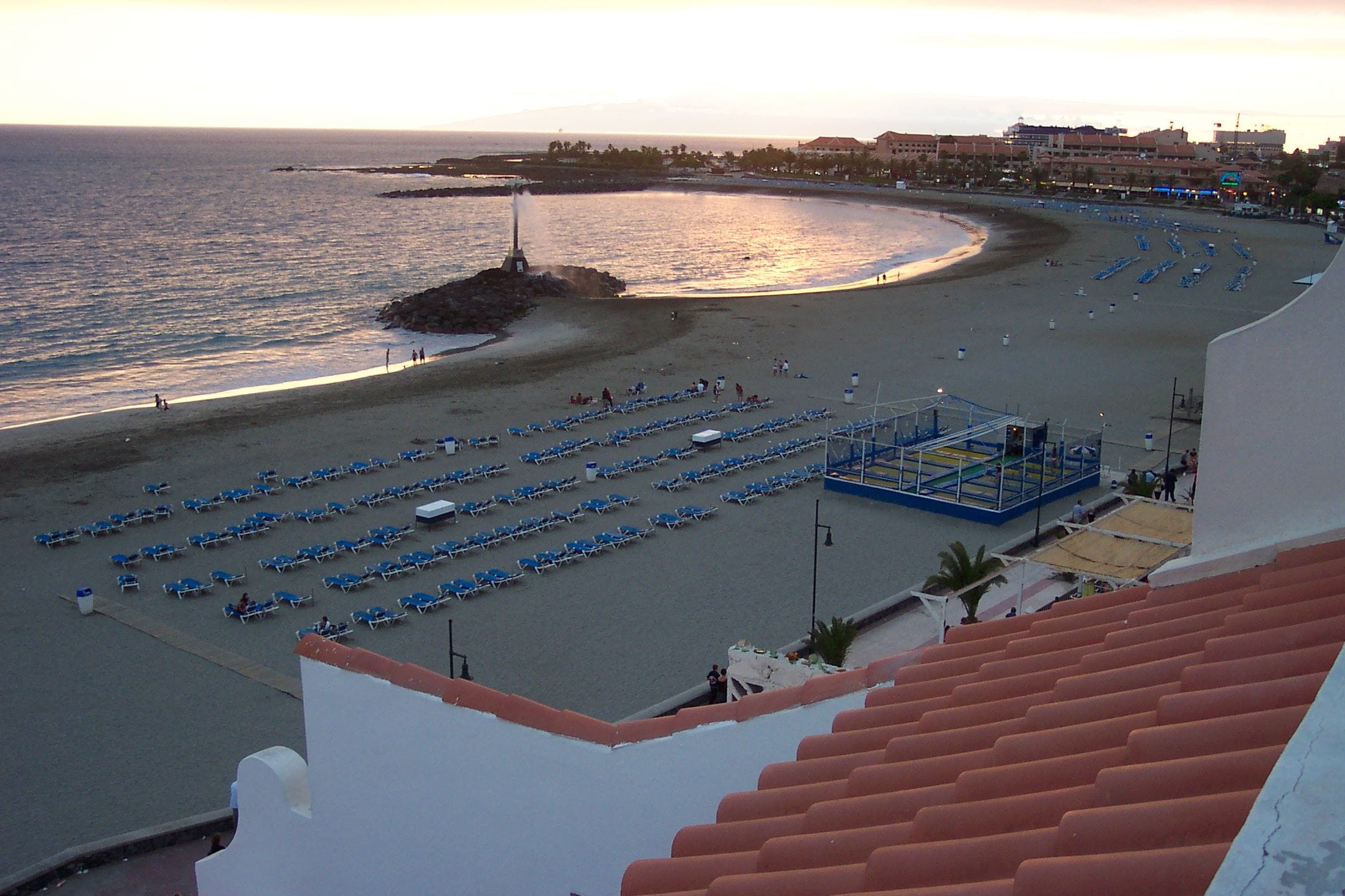 Una spiaggia con file di sedie a sdraio blu e alcune persone che passeggiano.