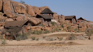 A desert landscape with rock formations and traditional thatched-roof huts. - Canyon Lodge (Fish River Canyon)