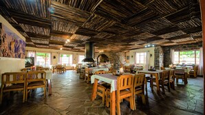 A rustic dining area with wooden tables and chairs, stone flooring, and a thatched ceiling. - Canyon Lodge (Fish River Canyon)