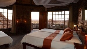 A room with a bed, a window with a view, and a stone wall. - Canyon Lodge (Fish River Canyon)