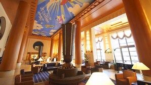A spacious lobby with a large central column, comfortable seating areas, and a mural of a rocket ship on the ceiling. - Disney Ambassador Hotel (Urayasu)