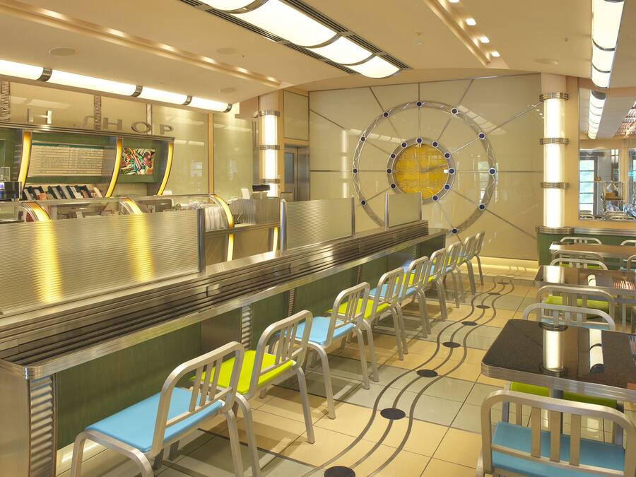 A modern restaurant with a long counter, seating area, and a decorative wall with a circular design.