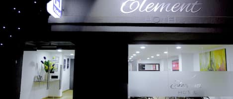 La entrada del Hotel Element, con un mostrador de recepción, un separador de vidrio y un área de descanso con sillas.