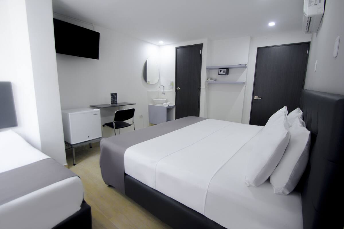 Una habitación de hotel moderna con una cama grande, un escritorio con una computadora, un lavamanos pequeño y un espejo.