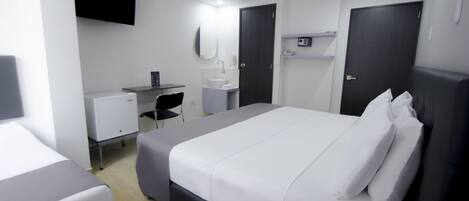 Una habitación de hotel moderna con una cama grande, un escritorio con una computadora, un lavamanos pequeño y un espejo.