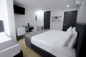 A modern hotel room with a large bed, a desk with a computer, a small sink, and a mirror.
