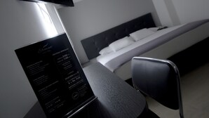 A hotel room with a bed, a desk, and a chair. There is a menu on the desk listing room rates and services.