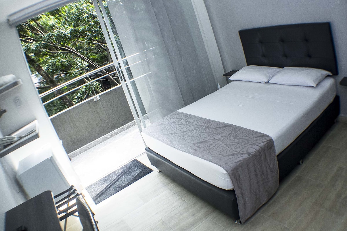 Un dormitorio moderno con una cama grande, una ventana con vista a árboles y un balcón con puerta.