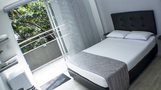 A modern bedroom with a large bed, a window with a view of trees, and a balcony with a door.