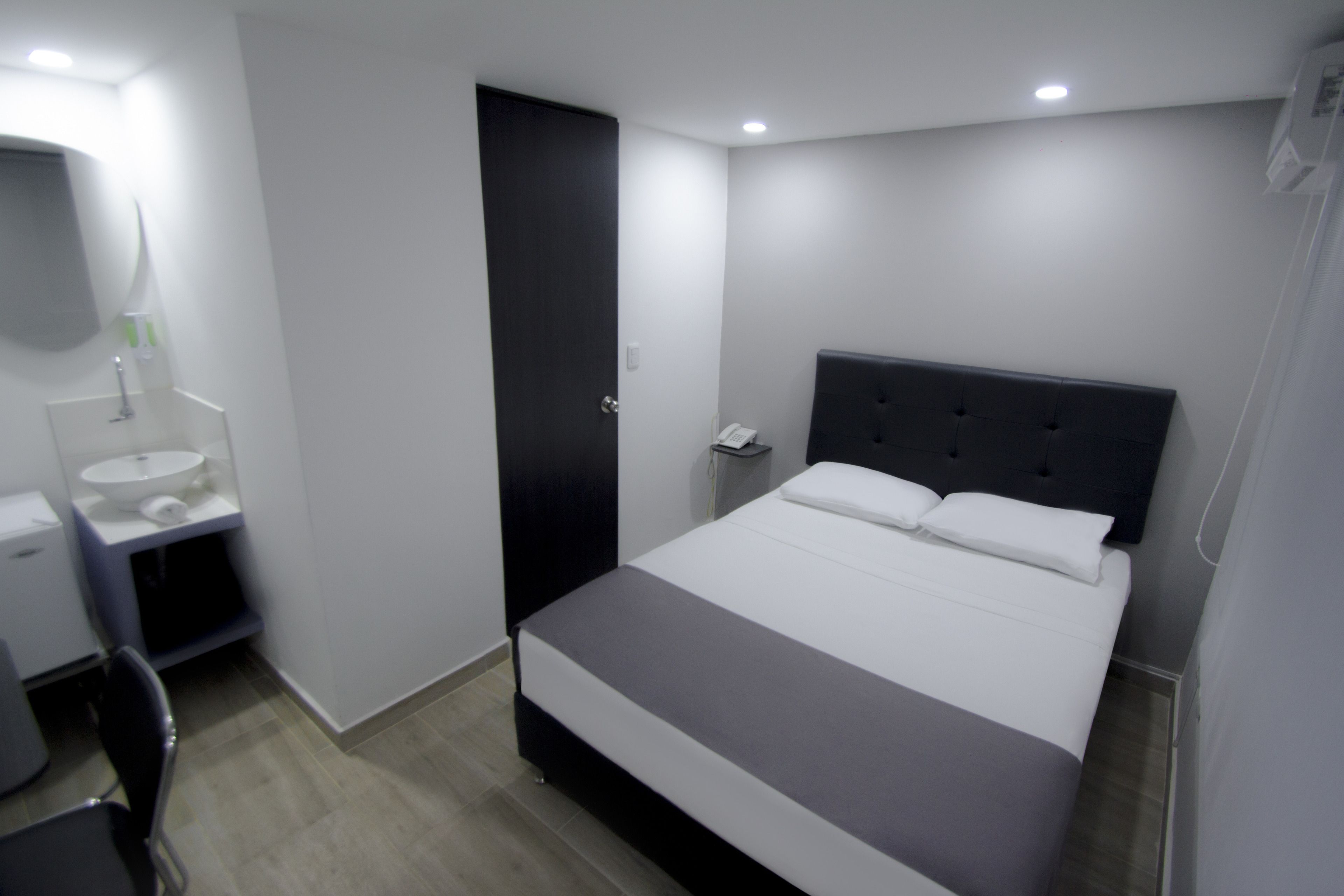 A modern bedroom with a large bed, a bedside table, a mirror, and a small bathroom area.