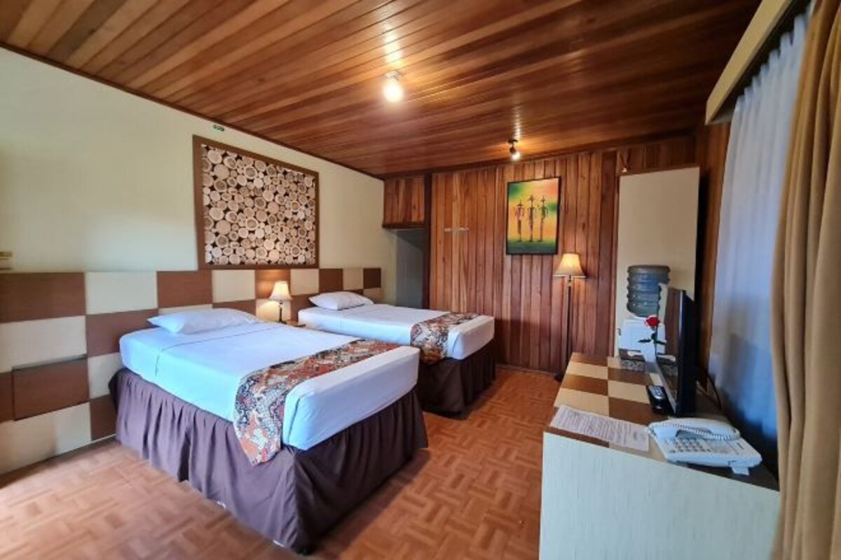A room with two beds, a desk with a telephone, and a wall-mounted TV.