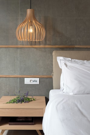 Une chambre moderne avec une table de chevet en bois, un lit blanc, un luminaire fixé au mur et une prise de courant.