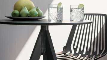 Una mesa con un plato de fruta y dos vasos de agua, una silla negra y una ventana que proyecta una sombra.