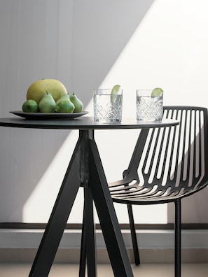 A table with a plate of fruit and two glasses of water, a black chair, and a window casting a shadow. - Ikones Seafront Luxury Suites (Rethymno)