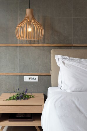 Een moderne slaapkamer met een houten nachtkastje, een wit bed, een wandlamp en een stopcontact.