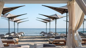 A beachside lounge area with rows of sunbeds under large umbrellas, overlooking the sea. - Ikones Seafront Luxury Suites (Rethymno)