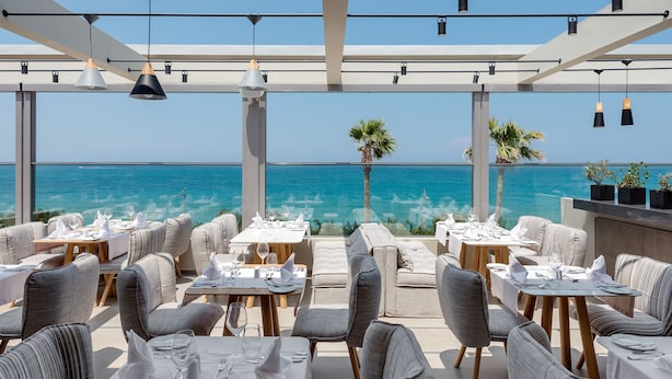 An outdoor dining area with tables and chairs, overlooking the ocean. - Ikones Seafront Luxury Suites (Rethymno)